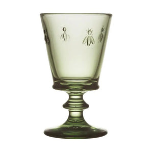 A table set for a meal features LA ROCHERE’s BEE WINE GLASS in Olive, along with clear glasses, plates, cutlery, and decorative greenery atop a white tablecloth.