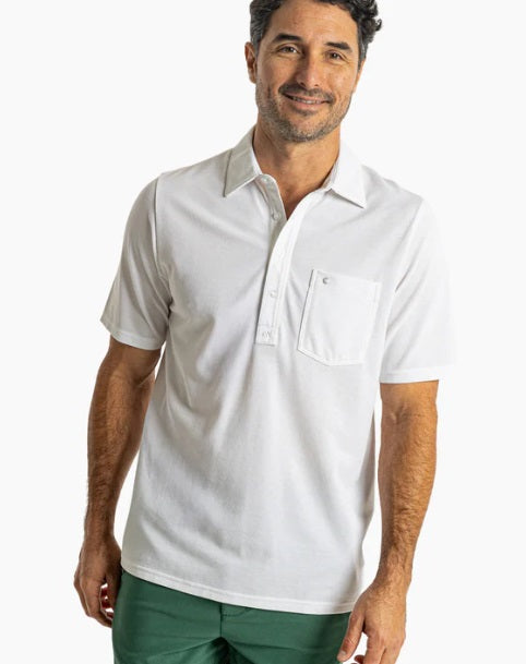 A man with dark hair and a short beard wears the CRIQUET Oxford Pique Players Shirt in white and green shorts, standing against a plain white background and smiling.