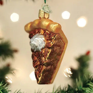 An OLD WORLD CHRISTMAS PECAN PIE ORNAMENT shaped like a slice of pecan pie topped with a dollop of whipped cream, hanging from a Christmas tree as a festive holiday dessert.