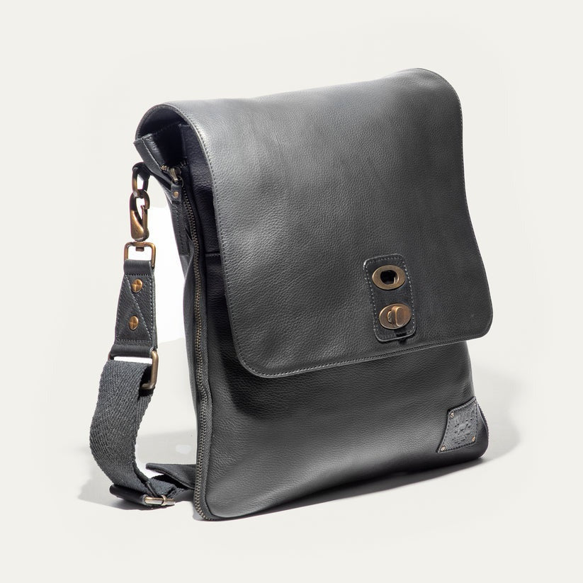 The WILL LEATHER GOODS OTTO Crossbody Bag in black full-grain leather features a front flap, gold-tone hardware, adjustable shoulder strap, and a small stitched patch on the lower right corner. Displayed against a plain white background.