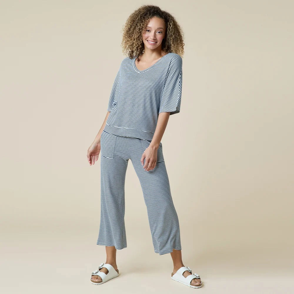 A woman wearing a light blue and white striped SOFTIES - DREAM RELAXED V-NECK WITH CAPRI LOUNGE SET with a V-neck, capri-length pants, and white sneakers.