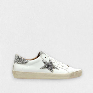 The MICHELE LOPRIORE - GEMMA SNEAKER WITH SILVER STAR by MICHELE LOPRIORE showcases smooth leather construction accented with a sparkling silver star on the side and a coordinating glittery heel tab. Set against a clean, light background, its ultra-light rubber sole features an intentionally worn finish that enhances its laid-back appeal.