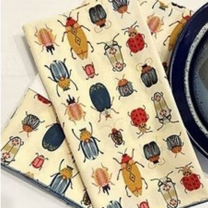 Introducing the DOT AND ARMY - BEETLE DINNER NAPKIN by DOT AND ARMY: a folded white cotton napkin adorned with a vibrant pattern of beetles and bugs in red, blue, yellow, and black hues, finished with blue edge stitching. Perfect as reusable napkins or charming beetle dinner accents for your table setting.