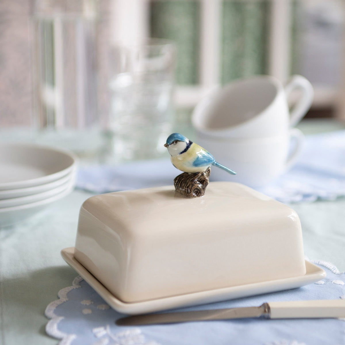 The QUAIL CERAMICS - BLUE TIT BUTTER DISH by QUAIL DESIGNS is a rectangular white butter dish with a lid, topped with a hand-painted blue and white ceramic bird as the handle.