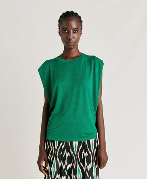 A person with braided hair is wearing a MOMONI ENNA LUREX JERSEY TOP and a skirt featuring a black, white, and green patterned design reminiscent of an 80s interpretation. The background is plain and neutral.