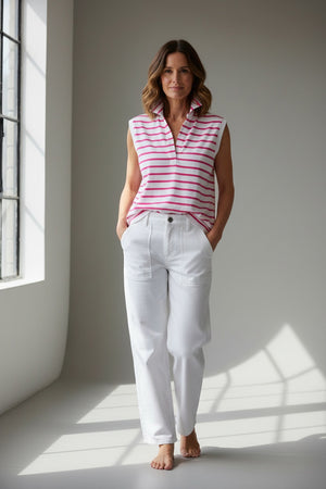 A woman with brown hair, wearing the FRANK & EILEEN Olivia Popover Henley Tank in Lotus Stripe and white pants, stands in a bright kitchen facing away, looking out a window.