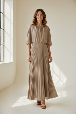 A woman poses against a plain background wearing the MOMONI - PARADISU DRESS by MOMONI, featuring light beige lurex jersey, kimono sleeves, and a pleated skirt. She styles it with braided hair, earrings, and open-toed shoes.