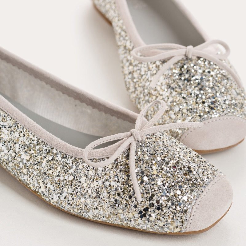 The REQINS HARMONY Sequin Ballerina Flat in Ice features a sparkling design with subtle pink trim and a small bow on the toe, shown from above against a plain light background.