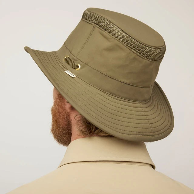 A man with a reddish beard and hair wears a TILLEY AIRFLO Medium Brim LTM5 hat in olive, offering UPF 50+ sun protection, and a beige button-up shirt, looking slightly to the side against a plain light background.