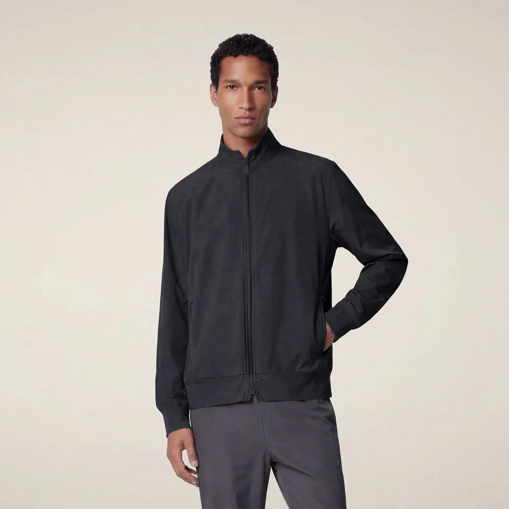 A person stands facing forward, wearing the SAVE THE DUCK - TULIO JACKET IN BLUE BLACK by SAVE THE DUCK, paired with gray pants and white sneakers, against a plain light background.