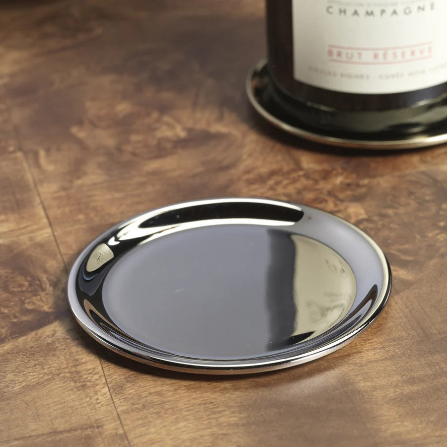 The ZODAX LOIRE WINE BOTTLE COASTER in a shiny nickel finish rests on wood, adding an elegant touch as it holds the base of a champagne bottle.