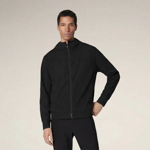 A man faces forward in the SAVE THE DUCK - LUIZ Hooded Jacket in Blue Black from SAVE THE DUCK, paired with black pants and white sneakers, set against a plain beige background.