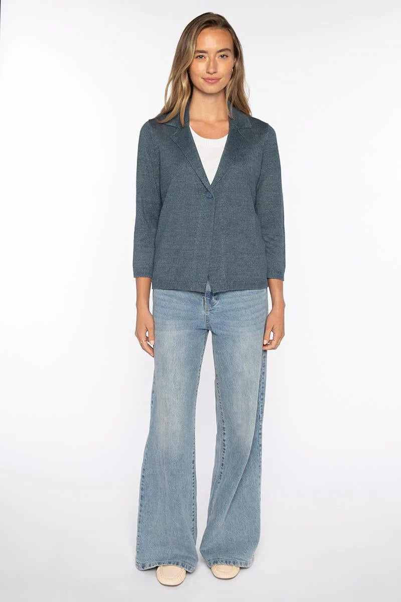 A woman stands facing forward against a white background, wearing the KINROSS EASY NOTH COLLAR LINEN CARDIGAN in blue over a white top, light blue flared jeans, and beige shoes.