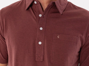 A man wearing the CRIQUET Top-Shelf Players Shirt in Mudslide Microstripe and beige pants stands with one hand in his pocket, smiling and looking to his left.