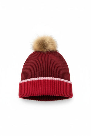 The MERSEA - Montauk Colorblock Beanie in Raspberry by MERSEA is a chunky knit red beanie with a folded brim, featuring a white stripe above the brim and finished with a light brown faux fur pom-pom, shown against a white background.