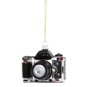 A black and silver GLASS CAMERA ORNAMENT by CODY FOSTER measuring 2.5 x 2 x 2.5 inches, hanging from a gold string.
