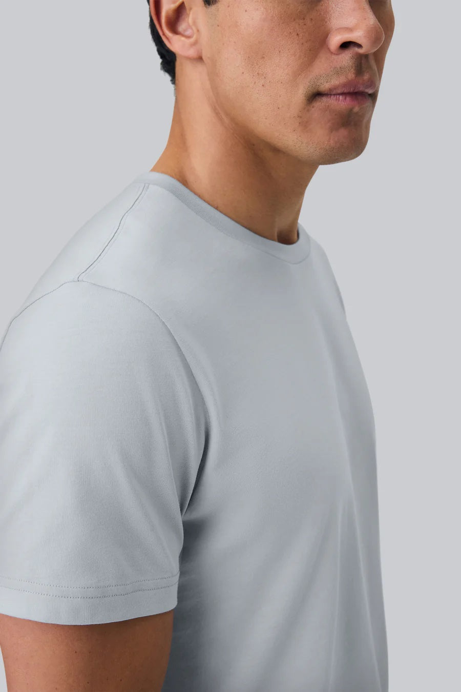 A man with short dark hair wears the MACK WELDON Pima Crew Neck T-Shirt in Steam and dark pants, standing against a plain light gray background and looking at the camera with a neutral expression.