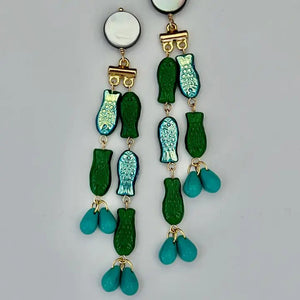 The SANDRINE FRANCE STUDIO - EVIE EARRINGS feature handmade round mother-of-pearl studs, gold connectors, green and blue fish charms, and turquoise teardrop beads at the ends.