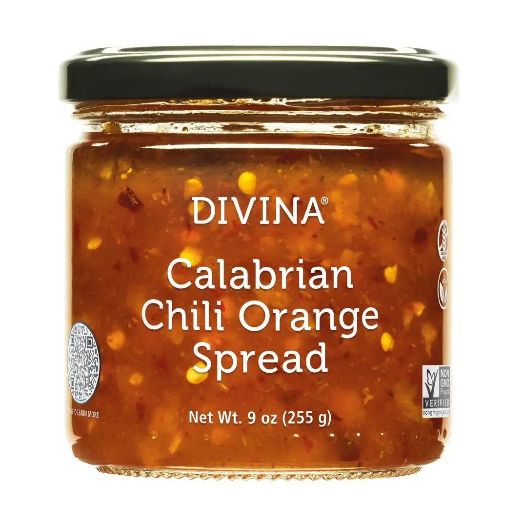 Two tortillas topped with shredded meat, red and green cabbage slaw, and cilantro sit on a wooden board with lime wedges on the side, placed on a purple cloth. A drizzle of DIVINA - CALABRIAN CHILI ORANGE SPREAD by DIVINA adds a sweet and spicy kick, perfectly complementing the vibrant flavors.