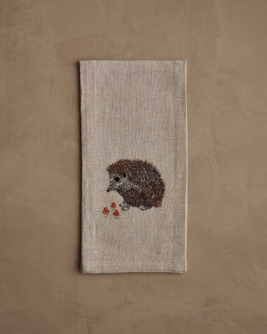 A HEDGEHOG WITH MUSHROOMS LINEN TEA TOWEL by CORAL & TUSK hangs from the handle of a white stove in a kitchen.