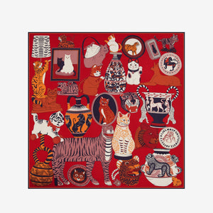 A woman with straight dark hair, dressed in a dark blazer, wears the luxurious INOUI EDITIONS - COLLECTIONNEUR SCARF WITH CATS IN MODAL SILK RED by INOUI. The red scarf—adorned with animal and wave designs and crafted from silk modal— is styled in a triangle around her neck as she stands against a plain white background.