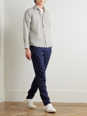 A person wears the HARTFORD - PAUL Linen Shirt in Army over a white tee and navy blue pants, standing against a plain light background.
