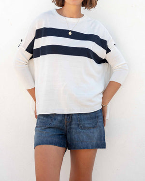Woman wearing the MERSEA - CATALINA CREWNECK SWEATER, white with two black stripes, paired with denim shorts and a gold necklace—an essential piece from MERSEA for effortless, versatile style.