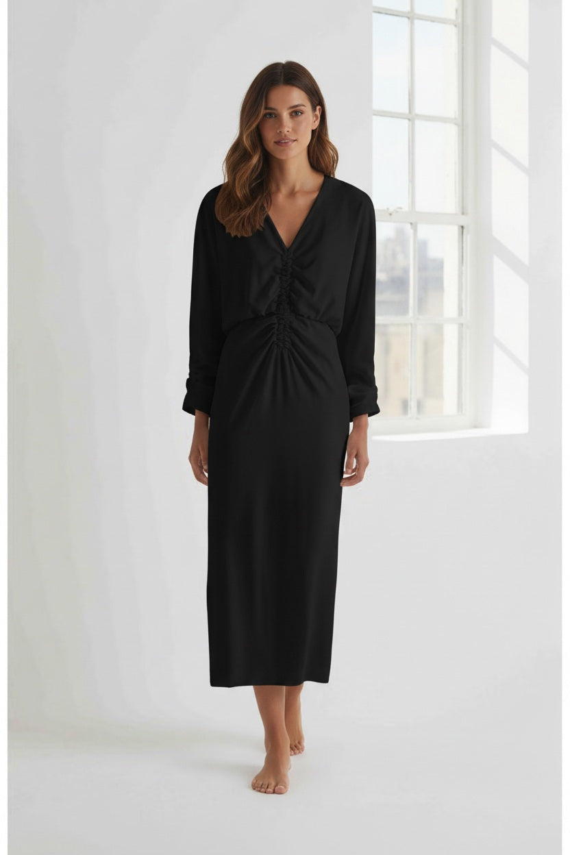 A person with short hair wears the MEIMEIJ Gathered Waist Long Sleeve Dress in Black, styled with dark sunglasses and black chunky shoes, standing against a plain white background.