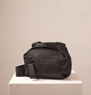 A person in a light beige suit carries the DANIELLA LEHAVI - BONNIE TRAVEL CROSSBODY, a large brown vegan bag with black zipper and strap, shown from shoulders to mid-thigh against a plain background.