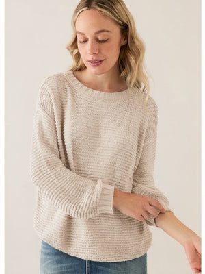 A woman with wavy blonde hair wears the BASE MILANO - CREWNECK COTTON BLEND SWEATER in light beige and blue jeans. She looks down, slightly smiling, touching her opposite sleeve against a plain light background.