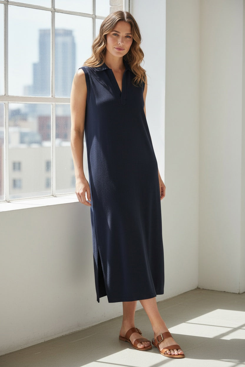 A woman wearing the FRANK &amp; EILEEN LILY Popover Henley Tank Maxi Dress in Vintage Jersey British Royal Navy and sandals stands smiling on a stone staircase outdoors, surrounded by green trees and sunlight.