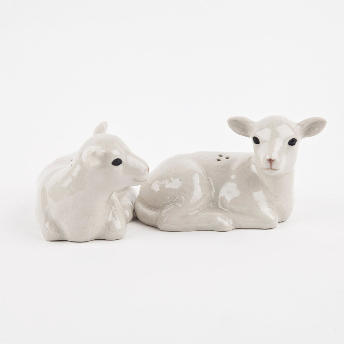 The QUAIL CERAMICS - LAMB SALT AND PEPPER SET by QUAIL DESIGNS features two hand-painted stoneware shakers shaped like lambs lying side by side, with a glossy finish and gentle expressions.