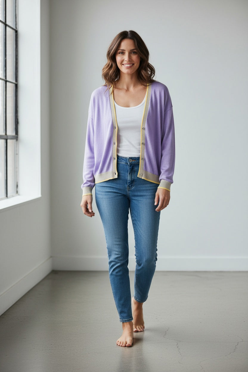 A woman wears the IN BED WITH YOU - BATWING SLEEVE CARDIGAN by IN BED WITH YOU/CLAUDIOLAI SRL, an orange V-neck with red and white trim, buttoned down the front, styled with multicolored patterned pants against a plain white background.