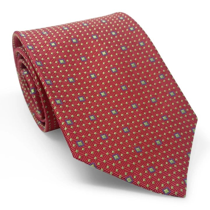 A close-up of the BIRD DOG BAY PETER-BLAIR - BESPOKE FINE SQUARES SILK TIE IN RED, a handmade silk tie featuring a red base with a geometric grid of small yellow and blue squares, finishing in a pointed tip.
