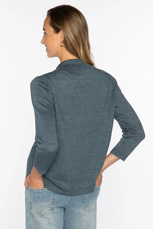 A woman stands facing forward against a white background, wearing the KINROSS EASY NOTH COLLAR LINEN CARDIGAN in blue over a white top, light blue flared jeans, and beige shoes.