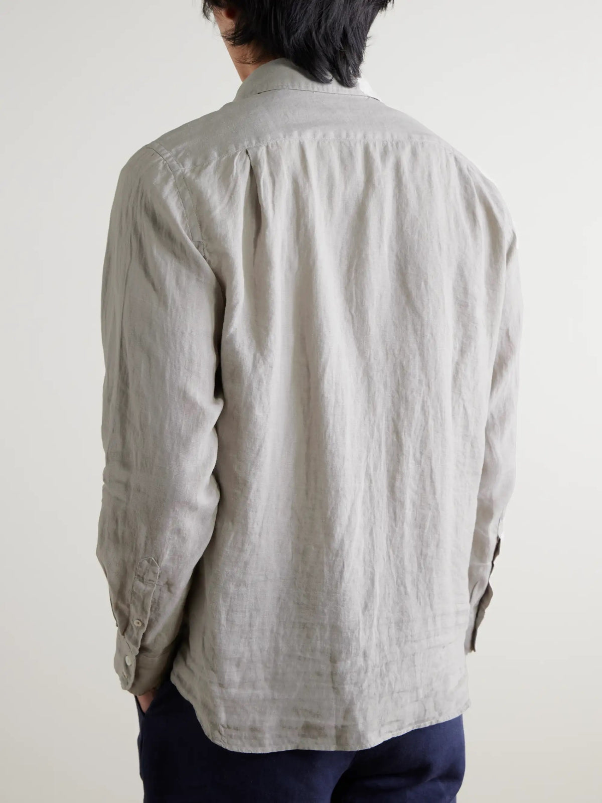 A person wears the HARTFORD - PAUL Linen Shirt in Army over a white tee and navy blue pants, standing against a plain light background.
