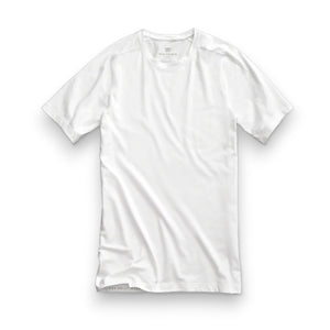 A man with short dark hair and a beard wears a slim fit white MACK WELDON - 18 HOUR JERSEY CREWNECK UNDERSHIRT and light blue pants, standing in profile against a plain light gray background.