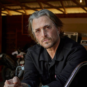 CADDIS - MABUHAY READING GLASSES by CADDIS feature a gold wire frame, large slightly tinted lenses, and brown plastic earpieces, crafted from nickel-free metal alloy and shown front-facing on a white background.