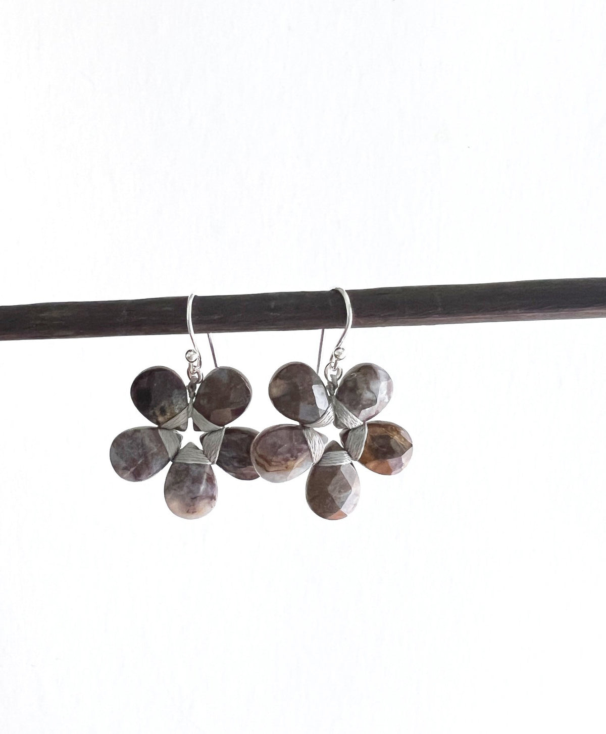 These sophisticated ANN LIGHTFOOT - Pietersite Flower Earrings showcase a graceful design with black petals complemented by sterling silver accents. Each earring is crafted with five symmetrical petals, exuding an elegant charm. Featuring convenient hooks for easy wearing, these earrings seamlessly blend style and functionality.