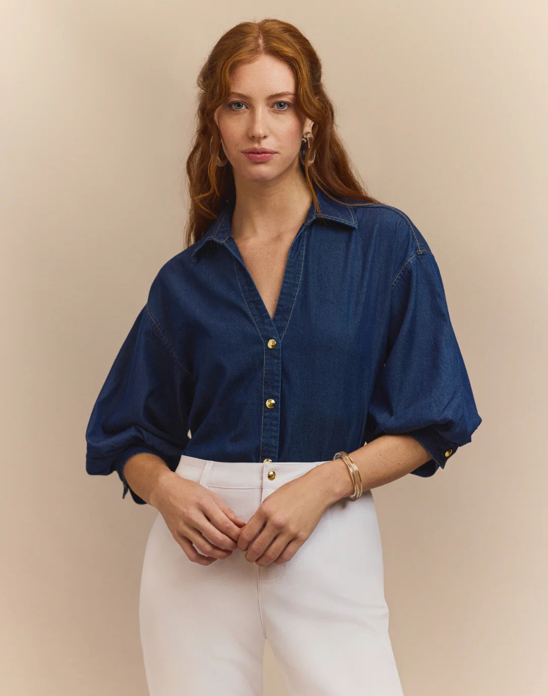 A woman with red hair faces away, wearing the HINSON WU Lilian Denim Elbow Sleeve Blouse in dark blue and white pants, set against a beige background.