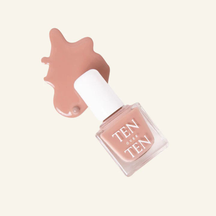 A glass bottle of TENOVERTEN - NAIL POLISH from the brand TEN OVER TEN, featuring a white cap and a dusty pink nail color. The front label displays "TEN OVER TEN" in white uppercase letters. This vegan, eight-free formula ensures both beauty and peace of mind. The background is plain and light-colored.