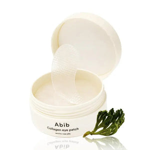 A white jar labeled "ABIB - COLLAGEN EYE PATCH JERICHO ROSE JELLY 60 PCS" from ASIAN BEAUTY WHOLESALE with a translucent eye patch being lifted—ideal for under-eye bags—sits beside a small green plant.