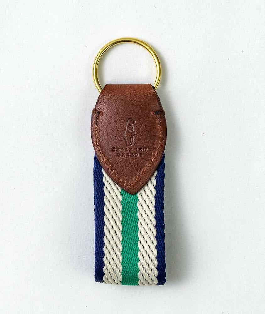 The BIRD DOG BAY COLLARED GREENS Dockside Key Chain features a gold ring, brown embossed leather with "COLLARED GREENS," and a woven strap in mint, white, and navy stripes. Proudly American Made.