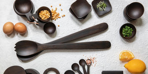 The BE HOME - Ebony Teak Streamlined Serving Set by BE HOME, INC features two hand-carved dark wooden utensils—a spoon and a jagged-edge spork—each with long handles, thoughtfully placed side by side on a white background. These elegant ebony teak servers add a modern touch to any dining table.