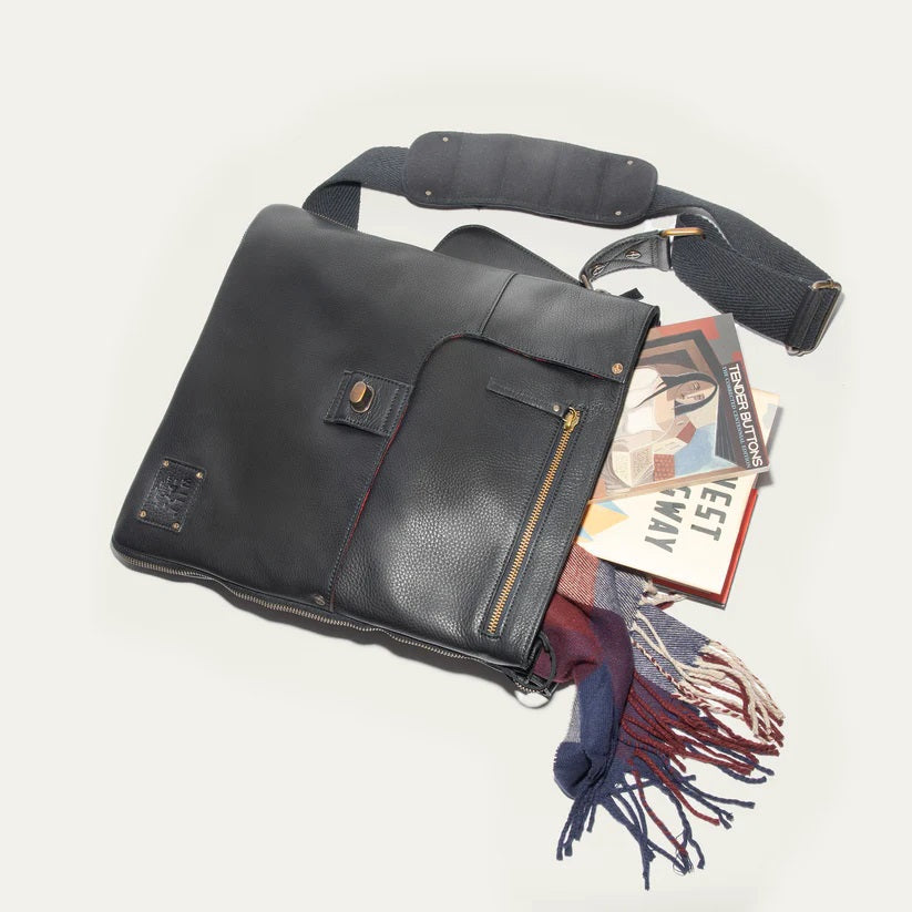 The WILL LEATHER GOODS OTTO Crossbody Bag in black full-grain leather features a front flap, gold-tone hardware, adjustable shoulder strap, and a small stitched patch on the lower right corner. Displayed against a plain white background.