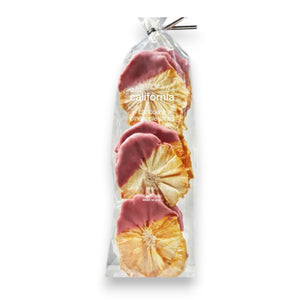 A clear plastic bag from DARDIMANS CALIFORNIA CRISPS contains several dried pineapple slices that are half-dipped in ruby chocolate. The label on the bag reads "DARDIMANS - RUBY CHOCOLATE PINEAPPLE SLICES." The bag, brimming with tropical sweetness, is secured with a twist tie and set against a textured, light grey background.