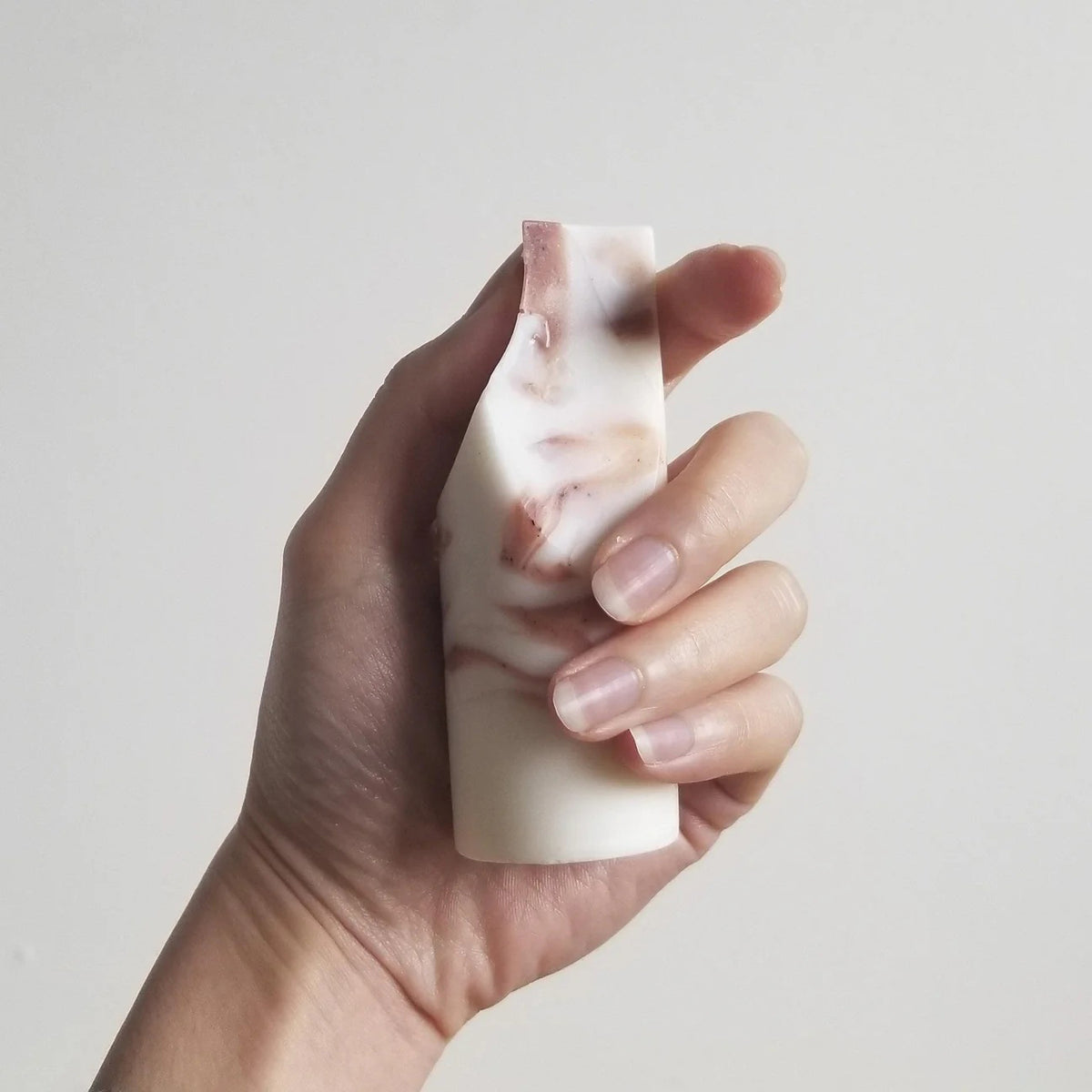 The UME - LAVENDER CREME MINI ERODE SOAP by UME STUDIO is a cylindrical bar with marbled white and brown swirls, standing upright on a white surface. Its top edge is slightly curved and uneven.