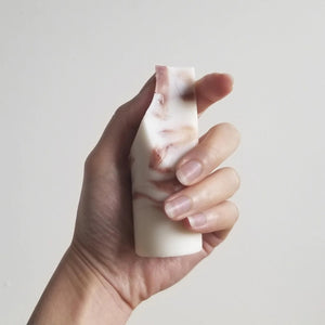 The UME - LAVENDER CREME MINI ERODE SOAP by UME STUDIO is a cylindrical bar with marbled white and brown swirls, standing upright on a white surface. Its top edge is slightly curved and uneven.