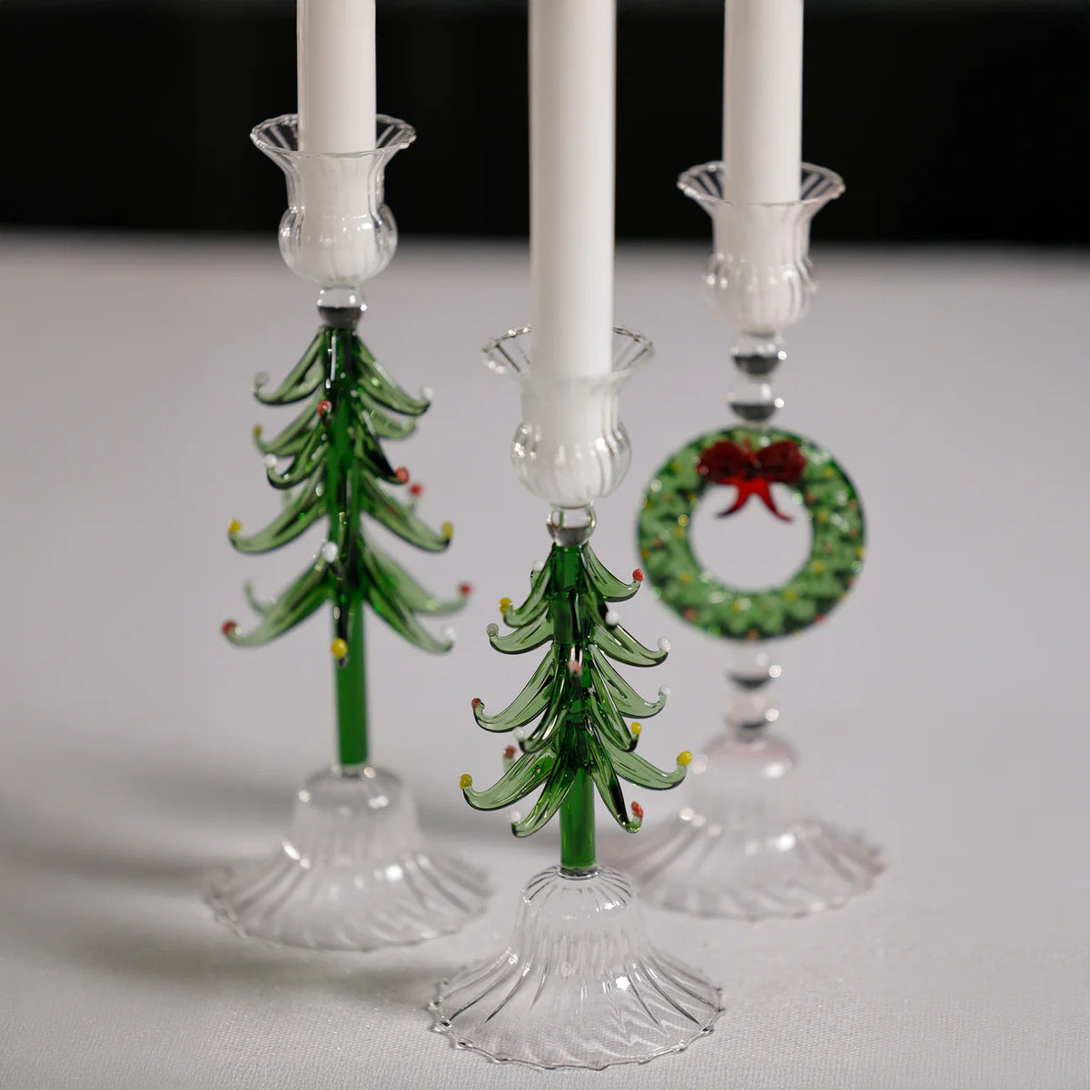 The ZODAX HOLIDAY TREE GLASS TAPER HOLDER is a clear glass candlestick shaped like a pine tree, featuring green branches, colorful ornaments, and a flared textured base. Dimensions: 3.25 in x 8.25 in.