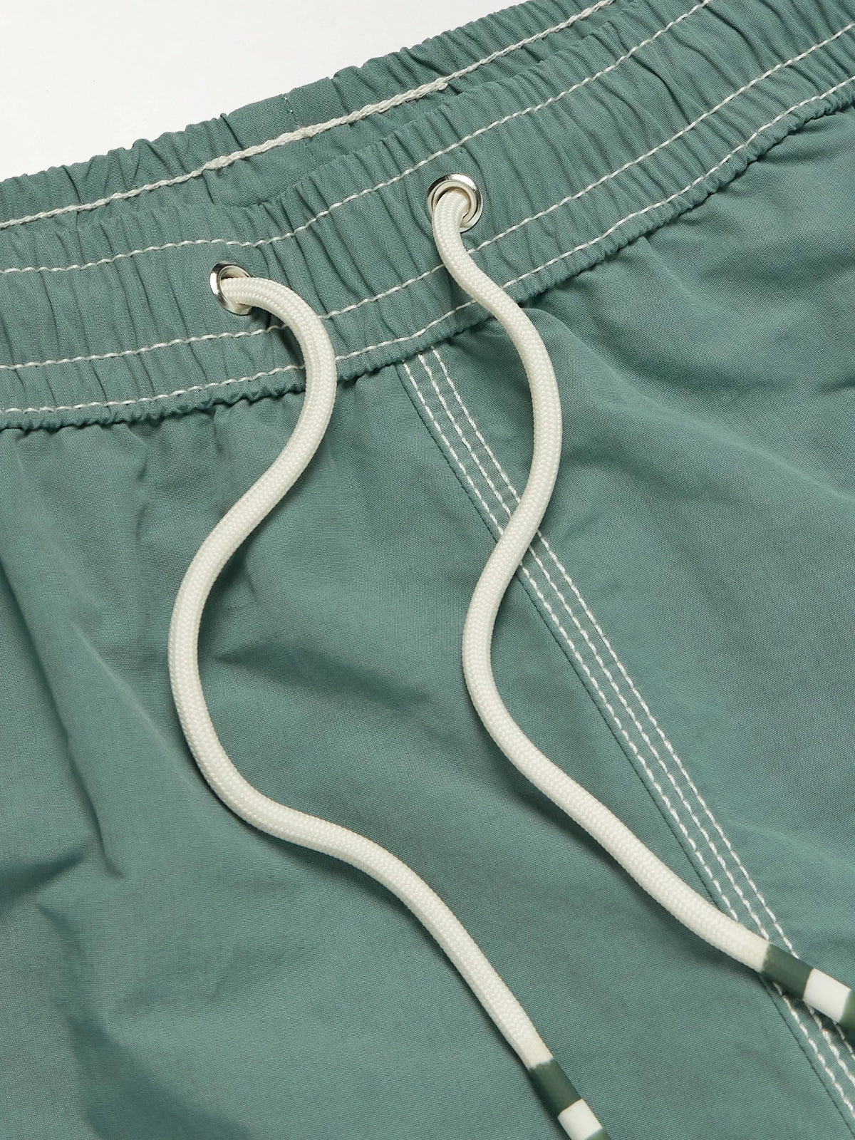 A pair of HARTFORD nylon swim trunks in Faded Kelly with white stitching and side pockets, shown flat on a light background. Includes travel pouch.